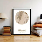 A framed map of India, specifically Mumbai, is displayed on a wall in a room with a stack of books and a lamp.