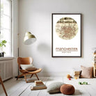 a cozy living room with a large framed map of Manchester hanging on the wall. The room has a comfortable seating area with a wooden chair and a floor lamp, and there are books and other decorative items scattered around the space.
