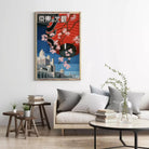 a living room with a large framed poster of a cityscape hanging on the wall, a gray sofa with a stack of books, and a small table with a plant.