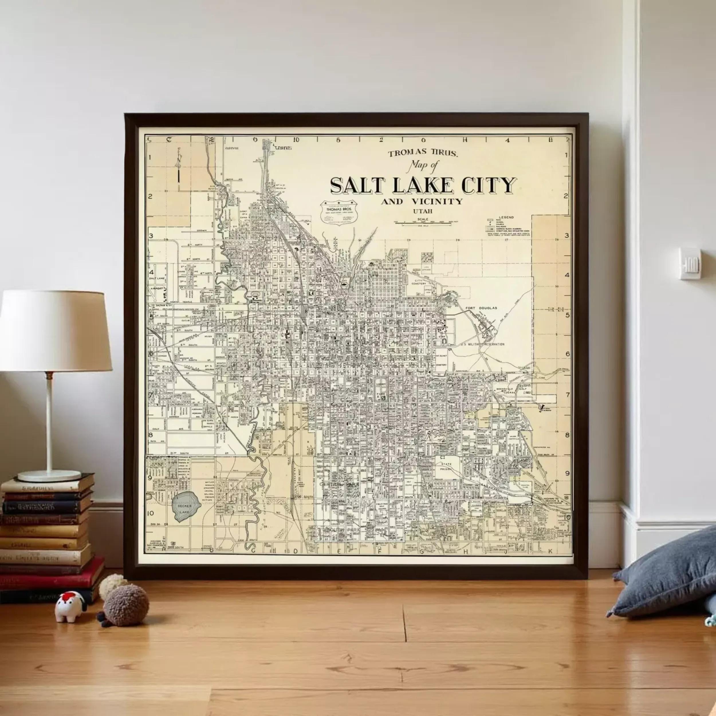 a framed vintage map of Salt Lake City, Utah, with a lamp and some books on a wooden floor in the foreground.