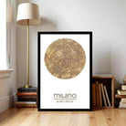 A framed poster of a map of Milan, Italy, displayed on a wall in a room with a lamp and bookshelf.