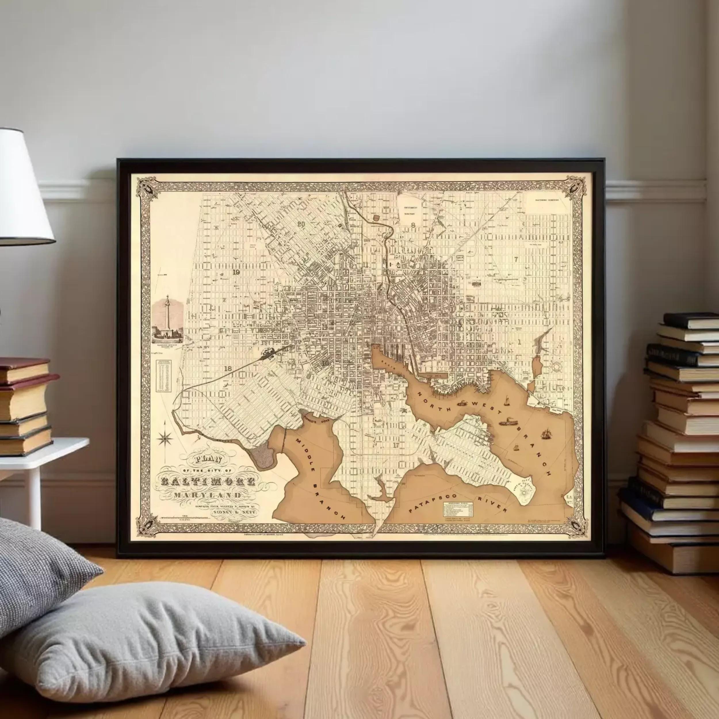 a framed antique map of Baltimore, Maryland, with a wooden floor and a stack of books in the background.