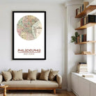 a framed map of Philadelphia hanging on a wall, with a bookshelf and a couch in the foreground.