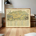 a large framed map of a city or region, with a wooden frame and a wooden floor. The map appears to be a detailed historical or geographical map, with various labels and markings. There are also several books stacked behind the map, suggesting a focus on historical or geographical information.