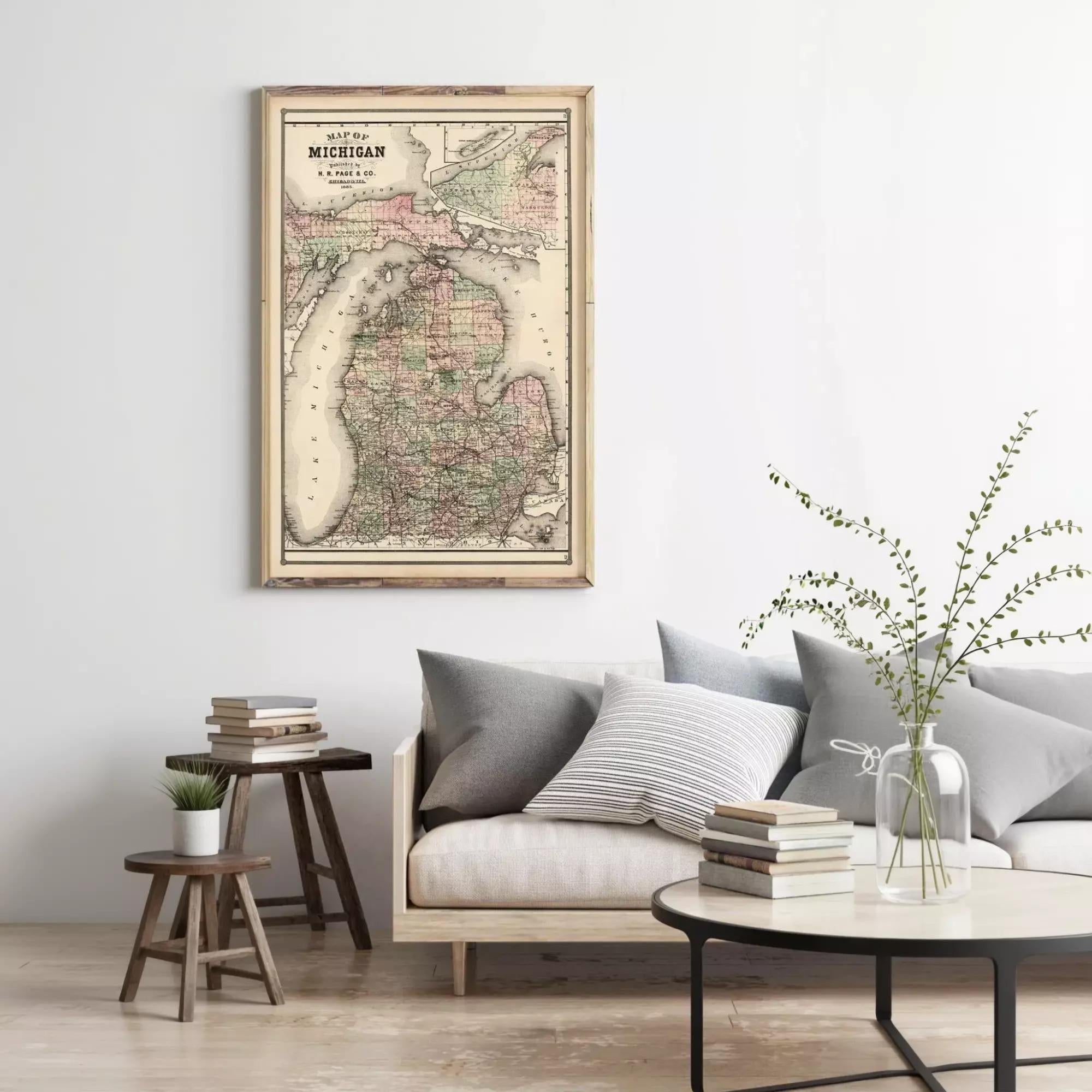 a living room with a framed map of Michigan hanging on the wall above a couch with pillows. There are also some books and a vase with greenery on the couch, creating a cozy and inviting atmosphere.
