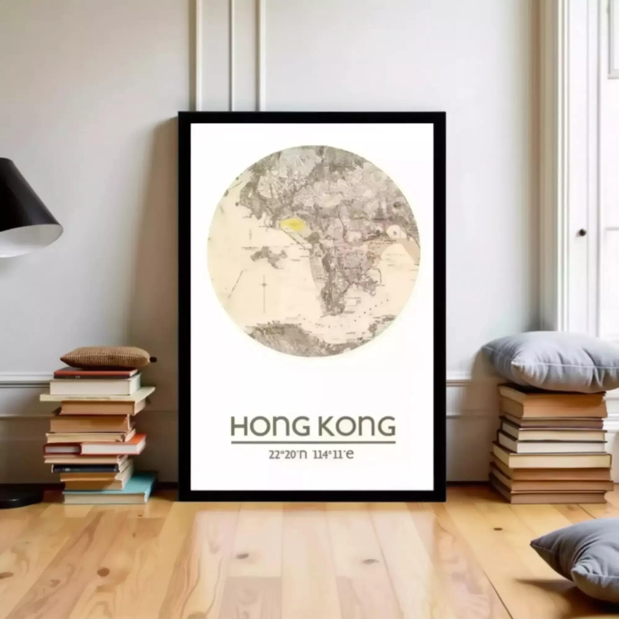 A framed poster of a map of Hong Kong, with the text "HONG KONG 22/20/11" printed on it, is displayed on a wall in a room with a stack of books and a lamp.