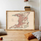 a large framed map of Trinidad and Tobago, with a wooden frame and a vintage map design. The map is displayed on a wooden floor, with a stack of books and a lamp visible in the background.