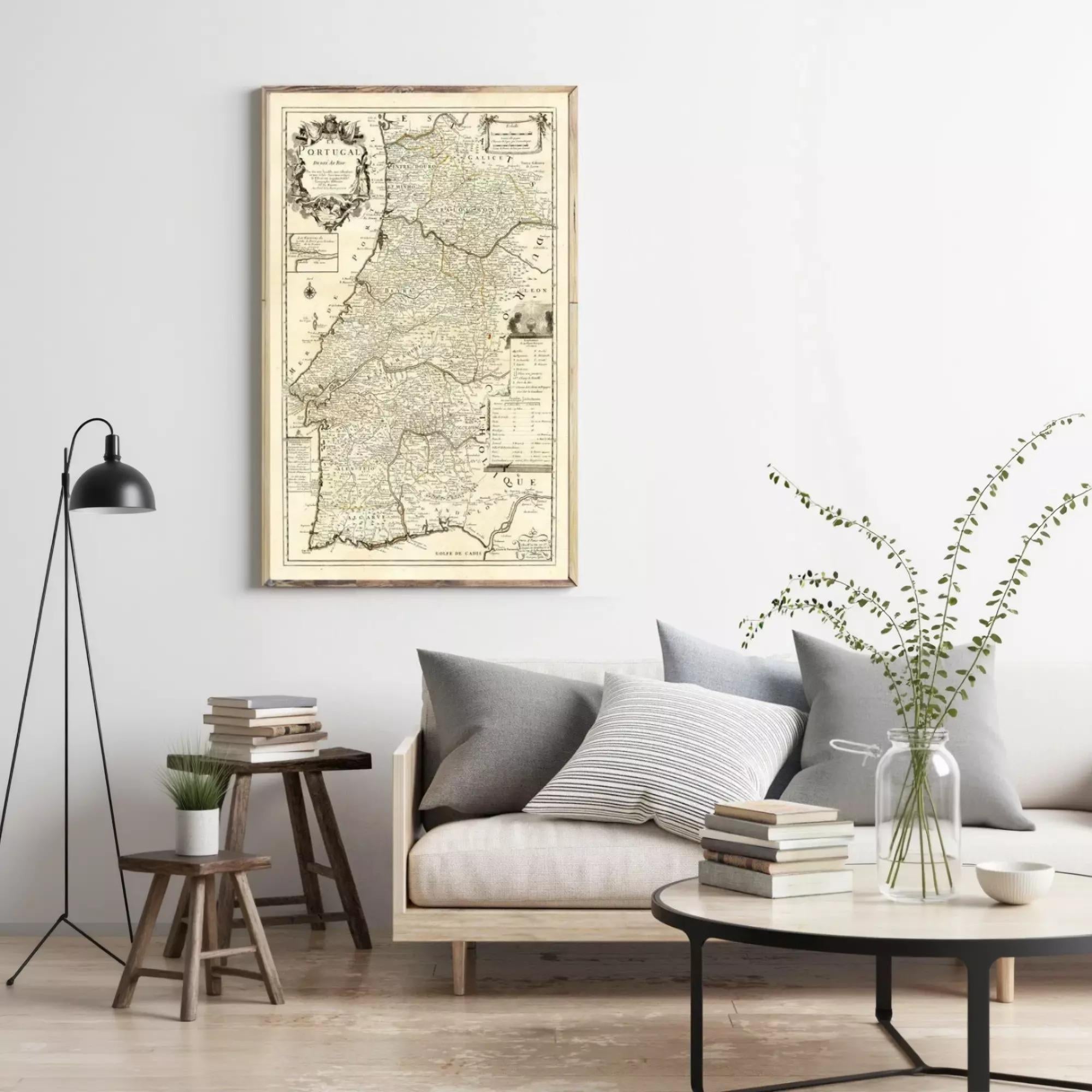 a living room with a large framed map hanging on the wall above a gray sofa with striped pillows. The room has a wooden coffee table, a side table with a plant, and a lamp. There are also several books and decorative items on the coffee table and side table.