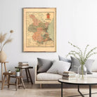 a living room with a framed map of Spain hanging on the wall above a couch with pillows. There are also some books and decorative elements in the room, such as a vase with greenery.
