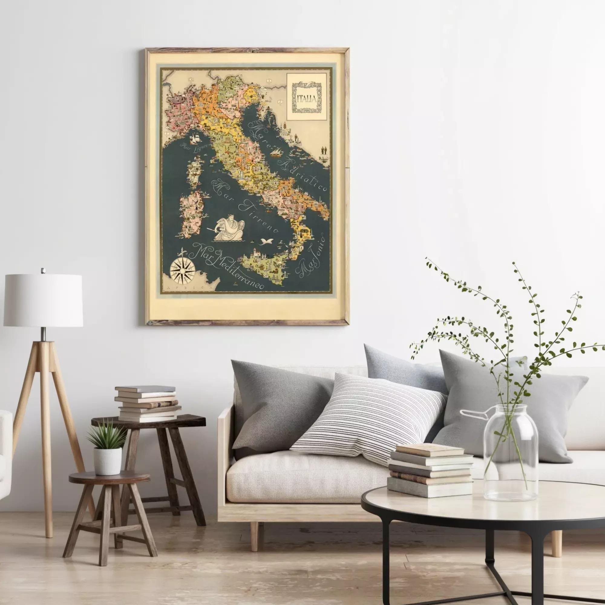 a living room with a large framed map of Italy hanging on the wall above a couch with pillows. There are also some books and a vase with greenery on the coffee table in front of the couch.