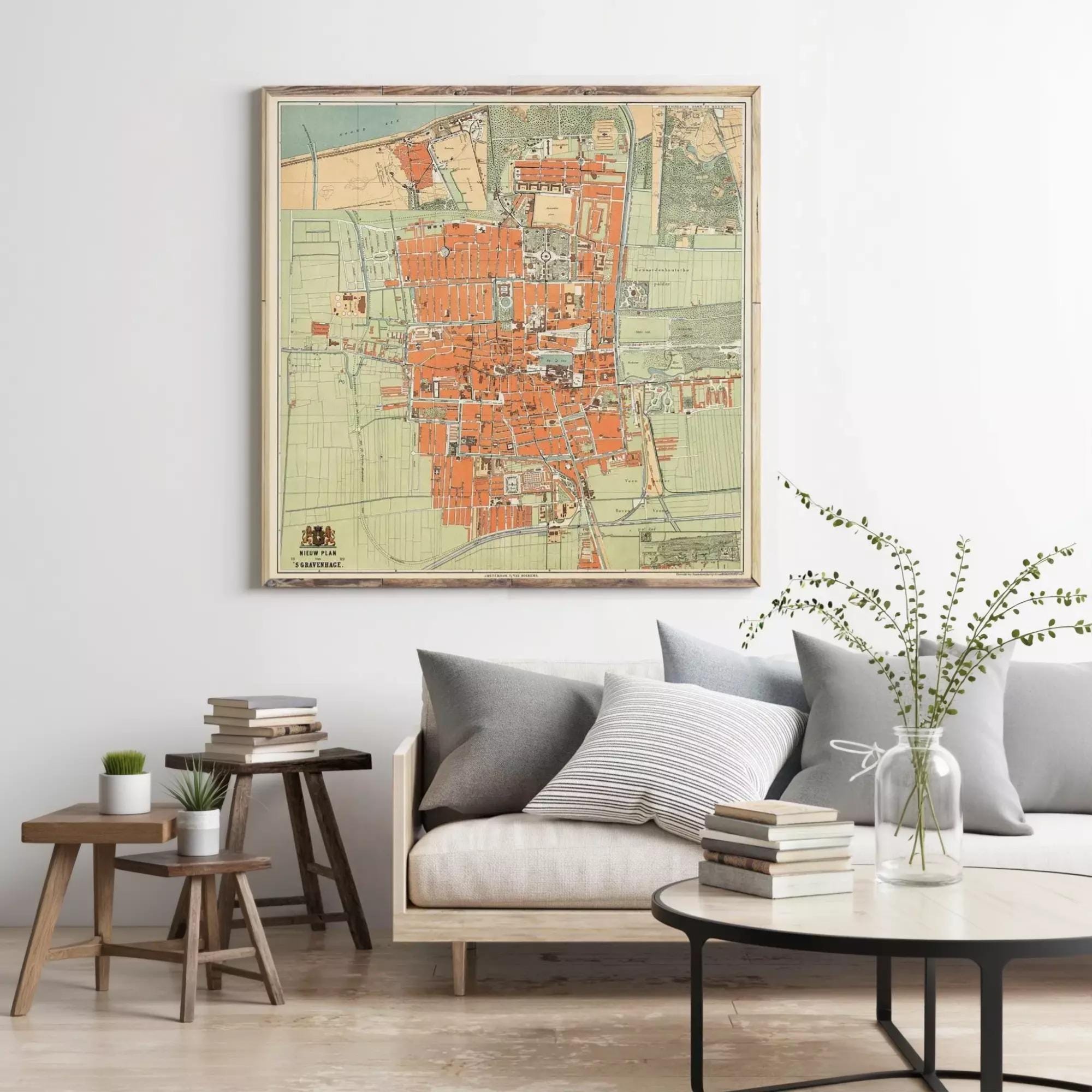 a living room with a large framed map of a city hanging on the wall above a couch with pillows. There are also some books and a vase with greenery on the coffee table in front of the couch.
