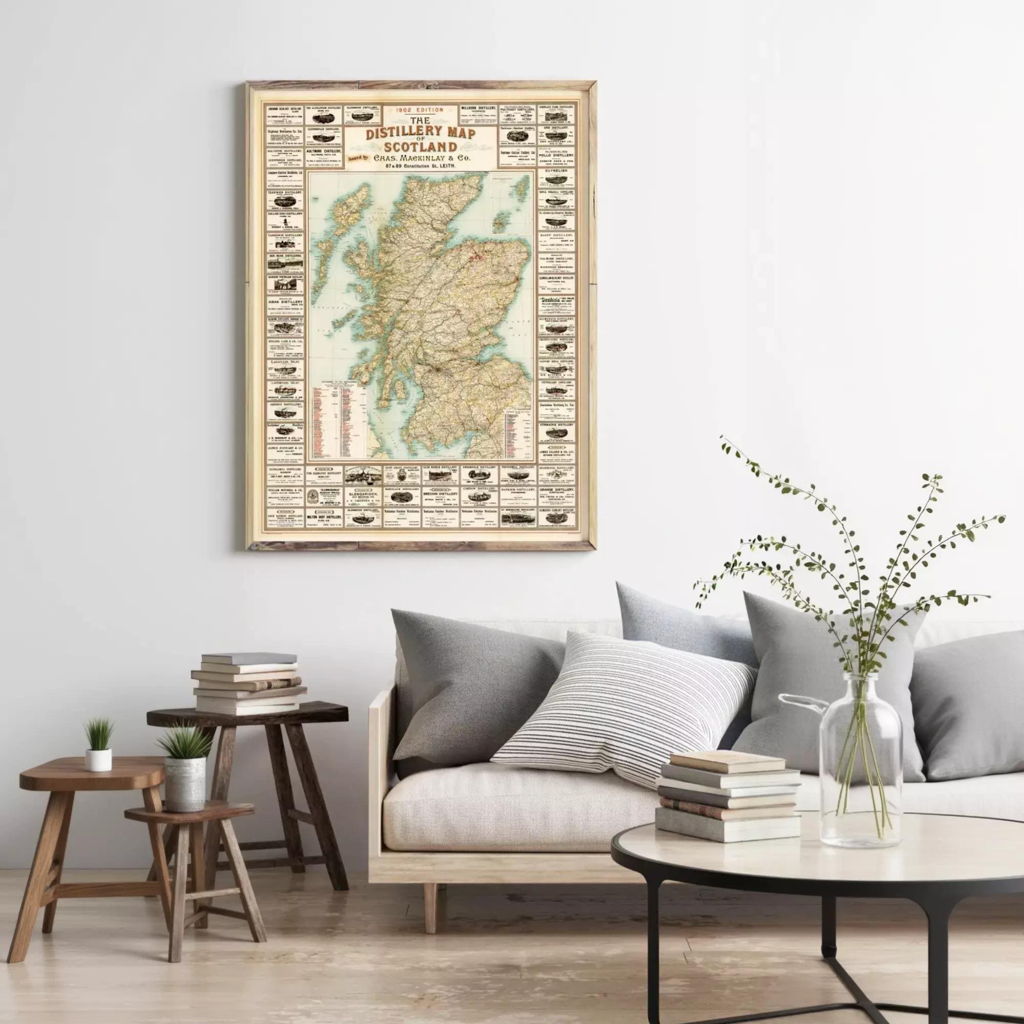 a living room with a large framed map of Scotland hanging on the wall above a couch with pillows. There are also some books and a vase on a table in the room.