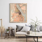 a living room with a large map of a city hanging on the wall, a wooden table with a vase of greenery, and a couch with a stack of books and a glass of water on it.