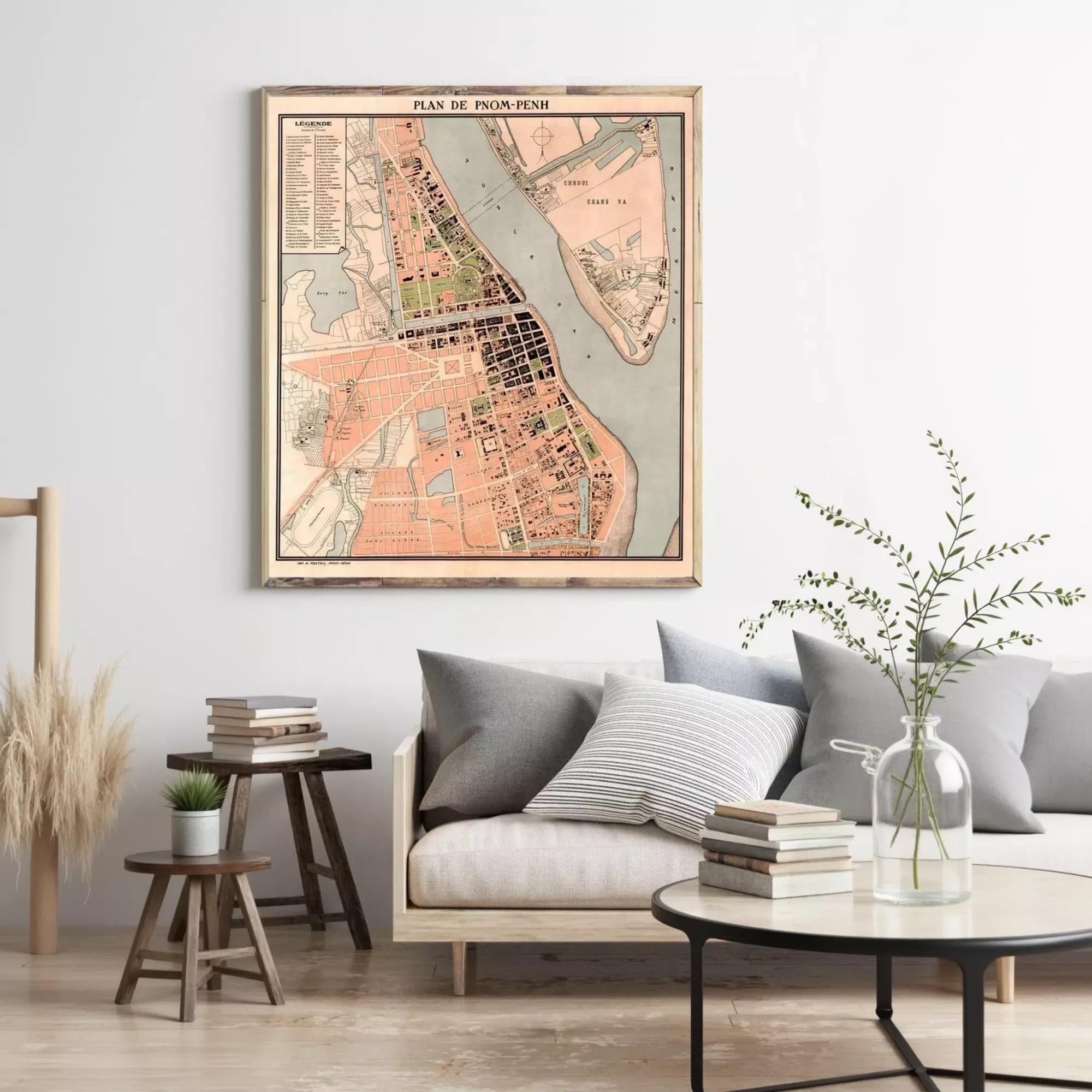 a living room with a large map of a city hanging on the wall, a wooden table with a vase of greenery, and a couch with a stack of books and a glass of water on it.