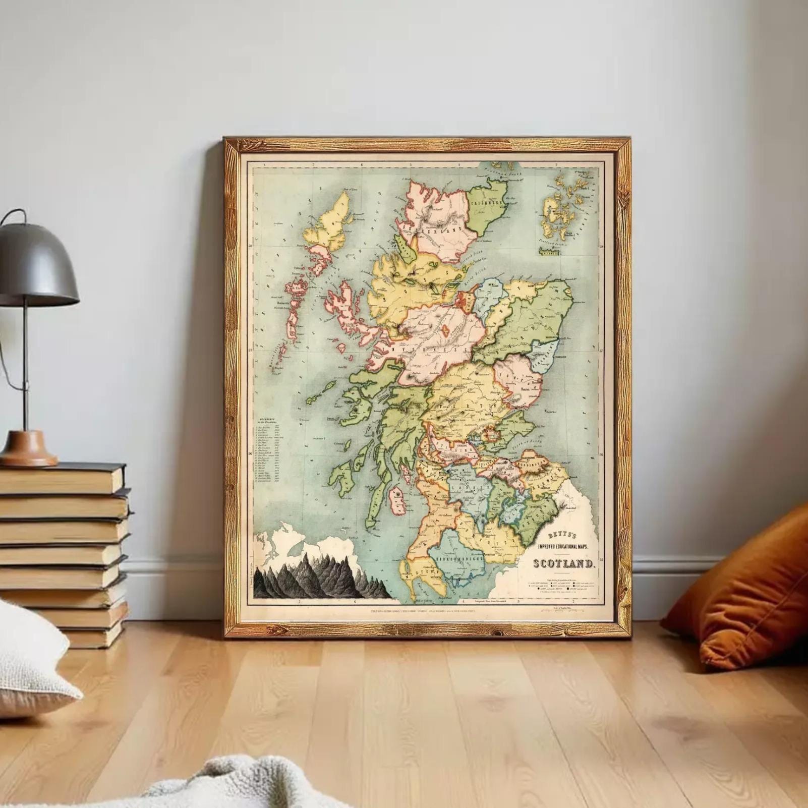 A framed vintage map of Scotland is displayed on a wall in a room with a lamp, books, and pillows.