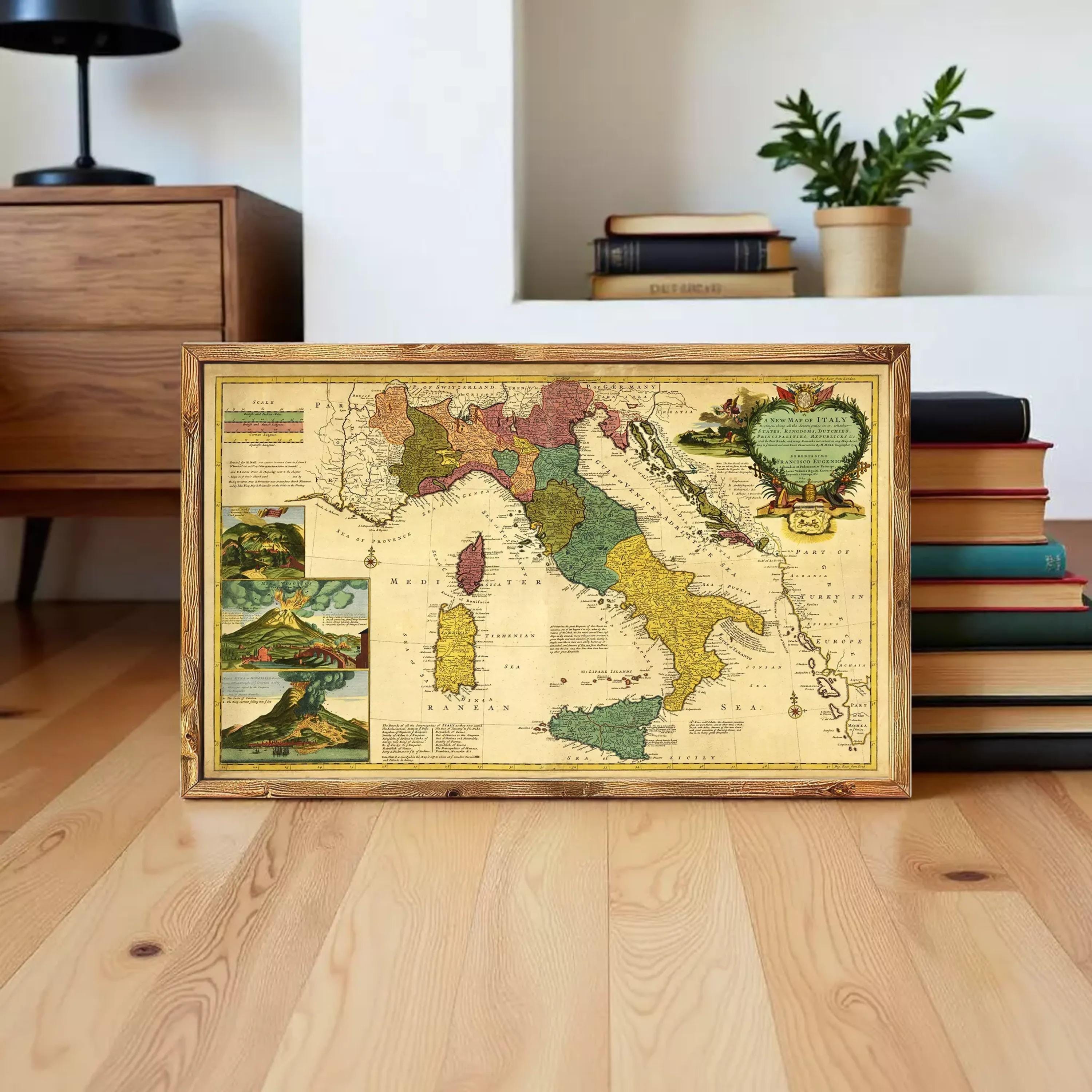 A framed vintage map of Italy is displayed on a wooden floor, surrounded by a stack of books and a potted plant.