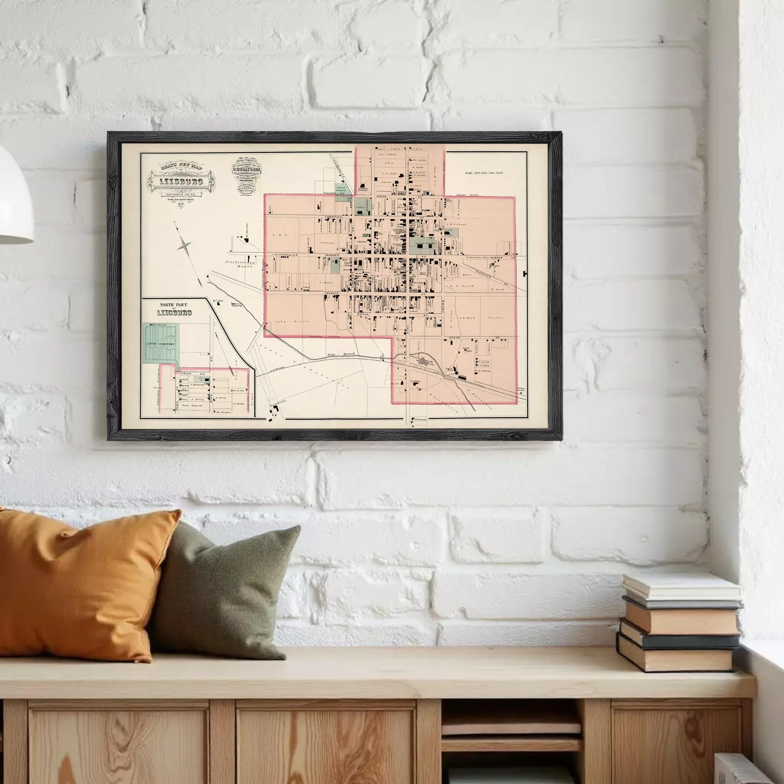 a framed map of a city hanging on a white brick wall, with a wooden bench and stack of books below it.