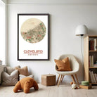 a cozy living room with a framed map of Cleveland, a white chair, a teddy bear, and a bookshelf filled with books.