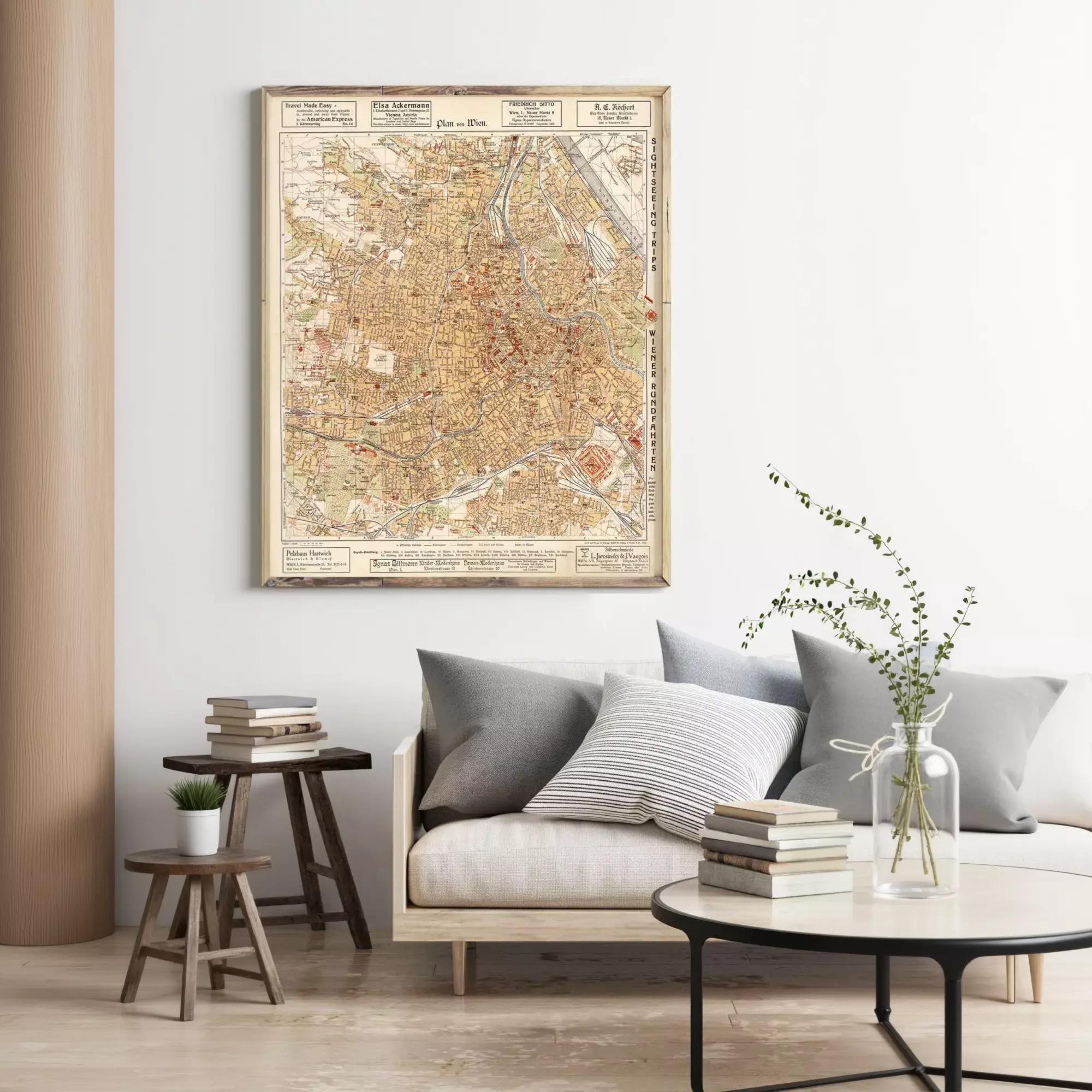 a living room with a large framed map of Paris hanging on the wall above a couch with pillows. There are also some books and a vase with flowers on the couch, creating a cozy and inviting atmosphere.