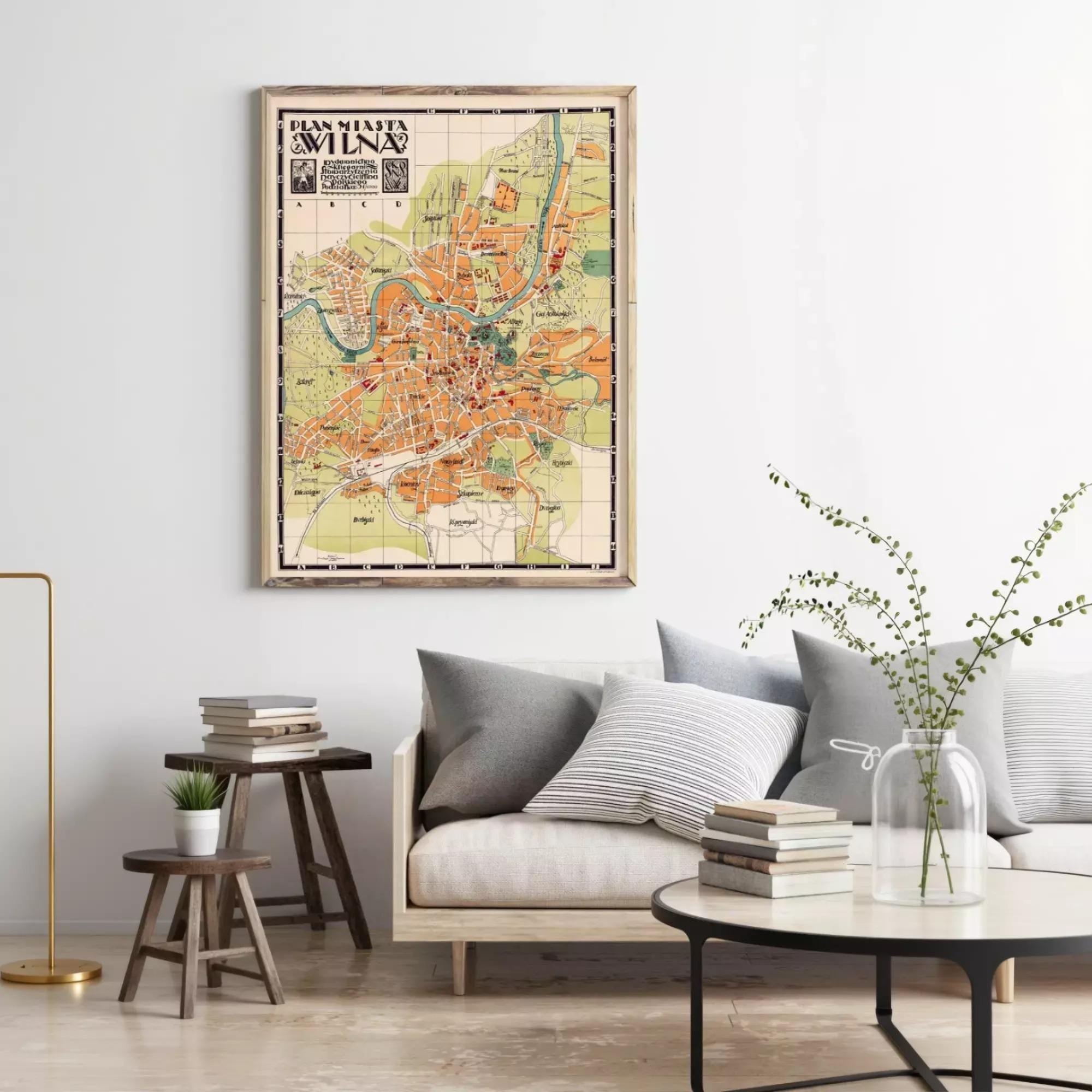 a living room with a large framed map of Milan hanging on the wall, a wooden stool, a sofa with pillows, a coffee table with books and a vase with flowers, and a potted plant.