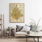 a living room with a large framed map of Indianapolis hanging on the wall above a couch with pillows. There are also some books and a vase on the coffee table in front of the couch.