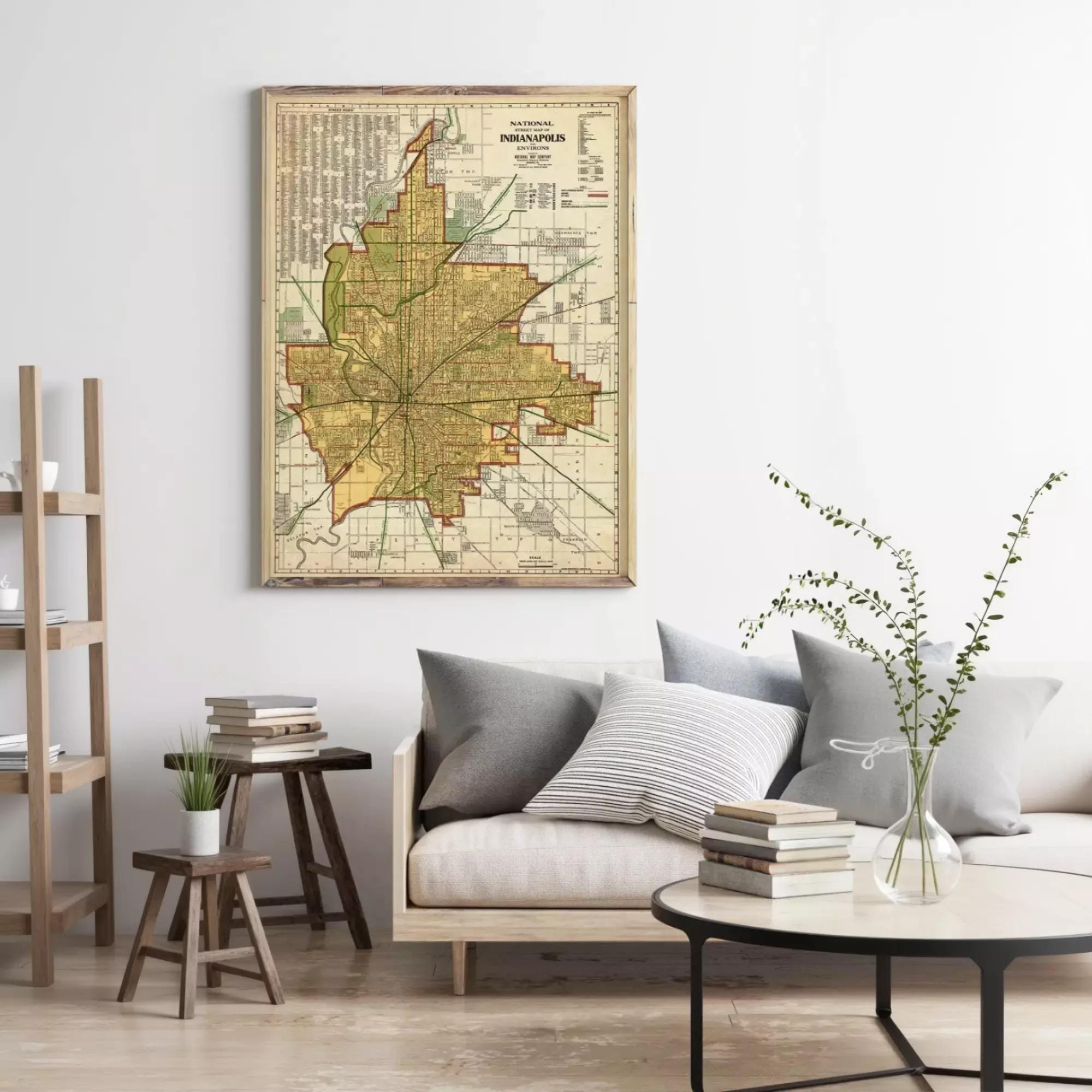 a living room with a large framed map of Indianapolis hanging on the wall above a couch with pillows. There are also some books and a vase on the coffee table in front of the couch.
