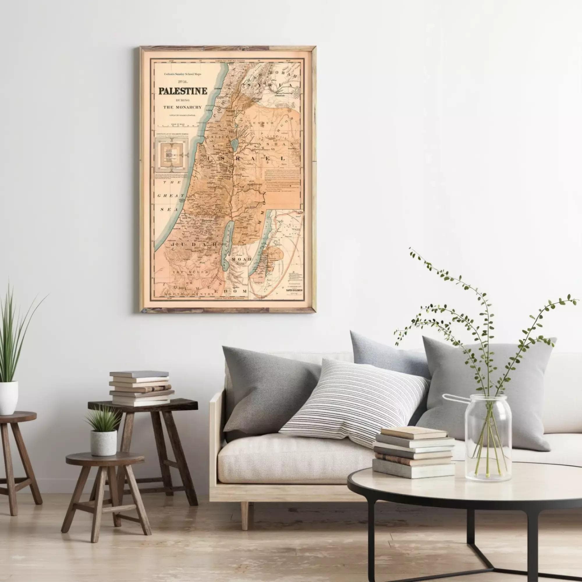a living room with a framed map of Palestine hanging on the wall above a couch with pillows. There are also some books and a vase with plants on the couch, creating a cozy and inviting atmosphere.