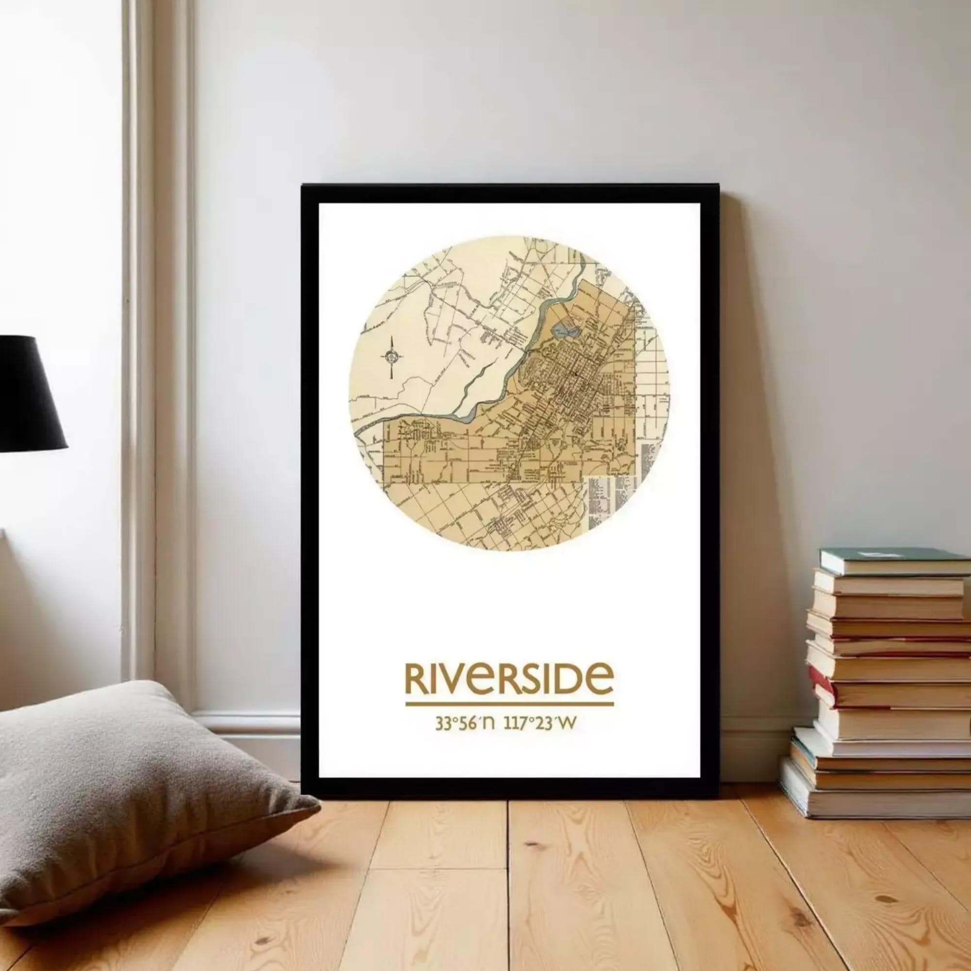 A framed map of the Riverside neighborhood, with a focus on the area around the river, is displayed on a wall in a room with a stack of books and a pillow.