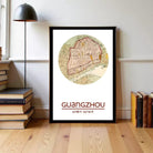 A framed map of Guangzhou, China, with the text "GUANGZHOU" and the date "23/09/13" printed on it, is displayed on a wooden floor next to a stack of books.
