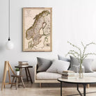 a living room with a large map of Europe hanging on the wall, a wooden stool, a round coffee table with books and a plant, and a gray couch with pillows.