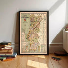 A framed map of Portugal is displayed on a wooden floor, surrounded by a stack of books and a few colored pencils.