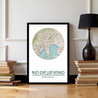 A framed map of Rio de Janeiro, Brazil, with a lamp and a stack of books on either side.