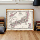 a framed map of Japan, with a wooden floor and a stack of books in the background.