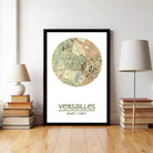 a framed map of Versailles, France, with a stack of books and a lamp on either side of it.