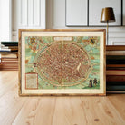 A framed map of a city, likely a historical or geographical map, is displayed on a wooden surface in front of a stack of books.