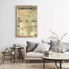 a living room with a framed map of the Texas Pacific Railway Way hanging on the wall. The room has a gray couch, a wooden side table, and a round coffee table with books and a vase of flowers on it.