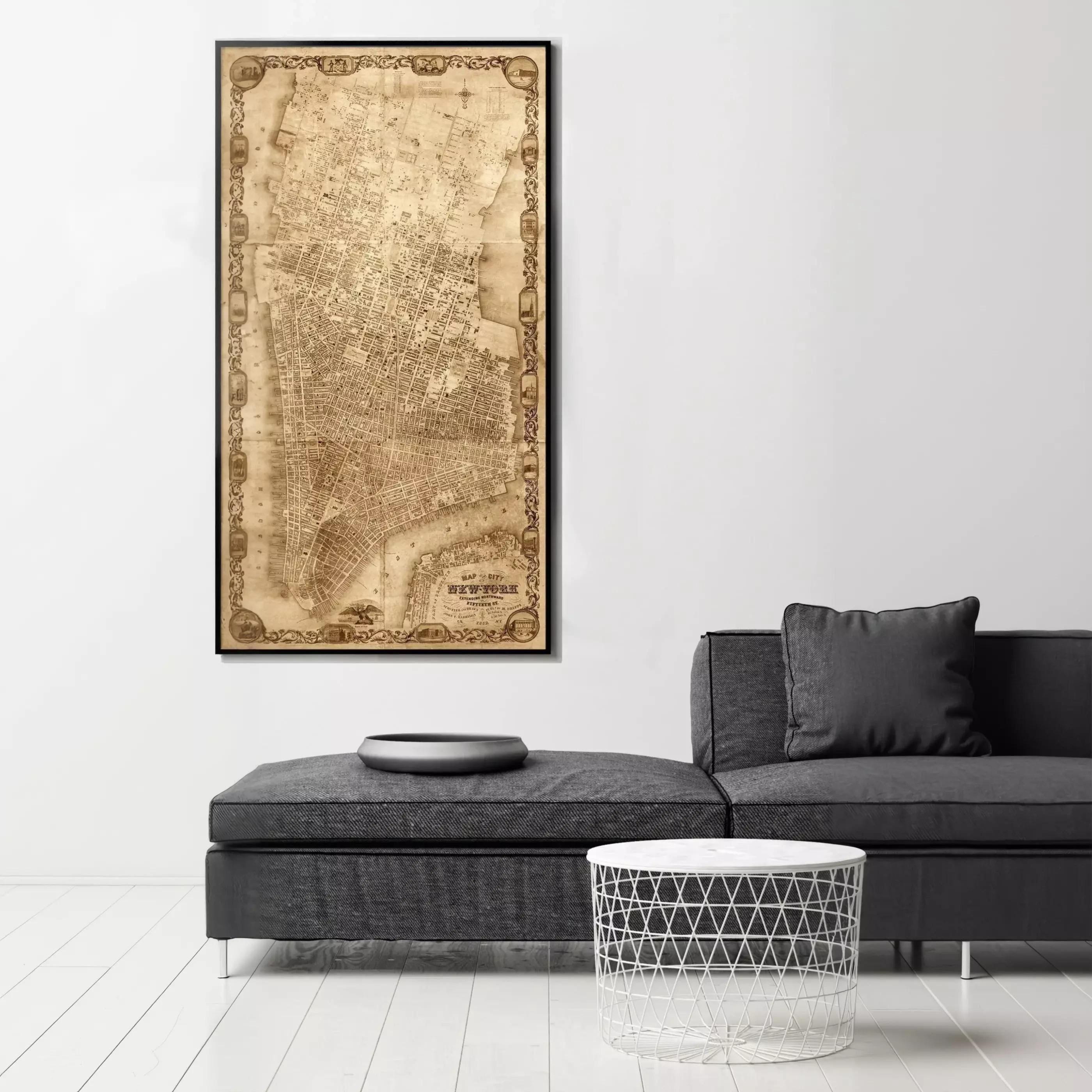 a large, ornate map of New York City hanging on a white wall above a gray sofa and a round table.