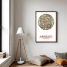 a framed poster of a map of Jerusalem hanging on a wall, with a lamp and pillows in the foreground.