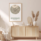 a wooden cabinet with a framed map of Amsterdam hanging on the wall above it. The cabinet has various items on top, including a potted plant, a vase, and some books. The overall setting appears to be a cozy and well-organized interior space.