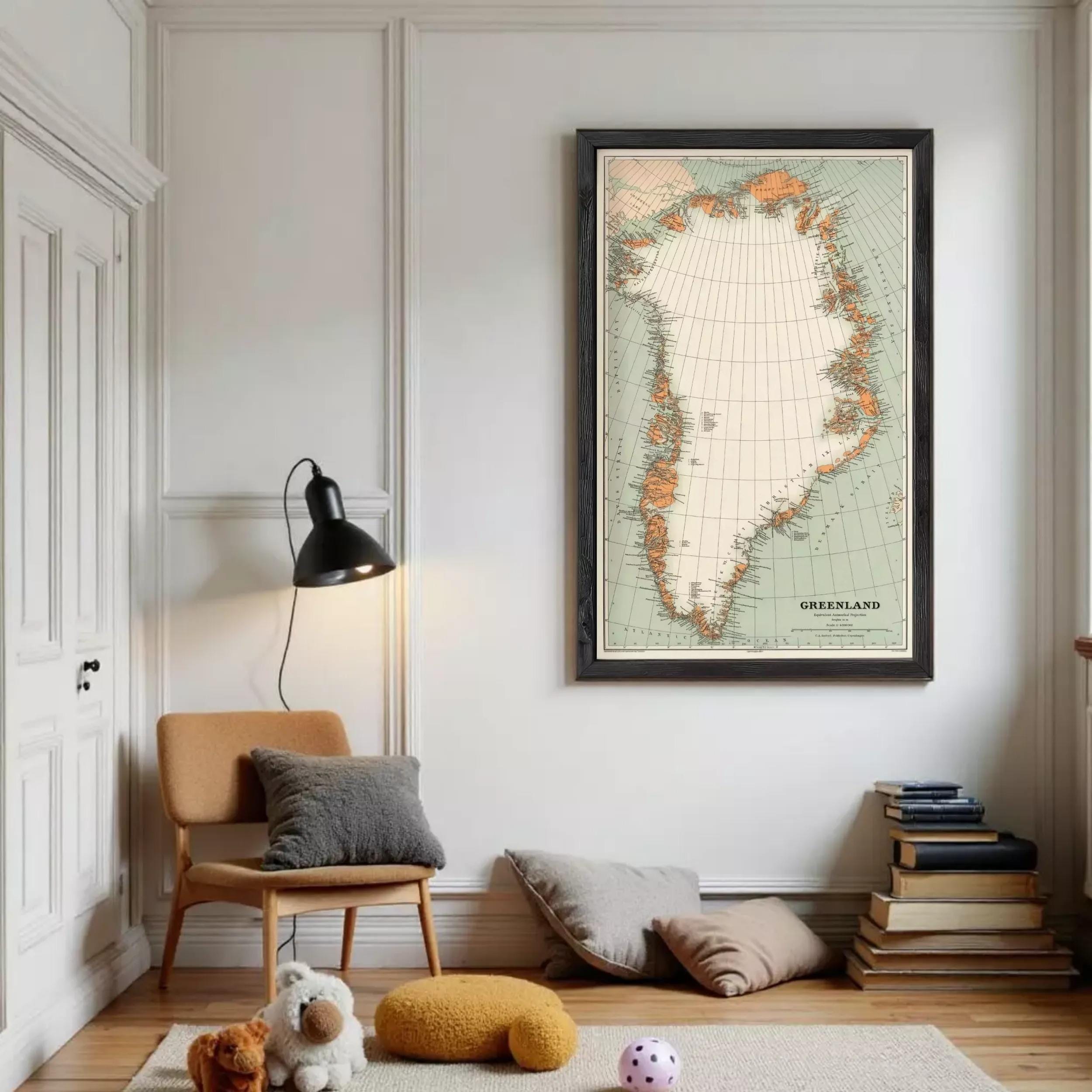 a cozy living room with a large framed map of Greenland hanging on the wall. The room is furnished with a chair, a lamp, and a stack of books. There are also some stuffed animals on the floor, adding a playful touch to the space.
