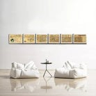 a minimalist living room with a white sofa and a small black table in the center. Above the sofa, there is a row of six framed artworks displayed on the wall, creating a cohesive and visually appealing arrangement.