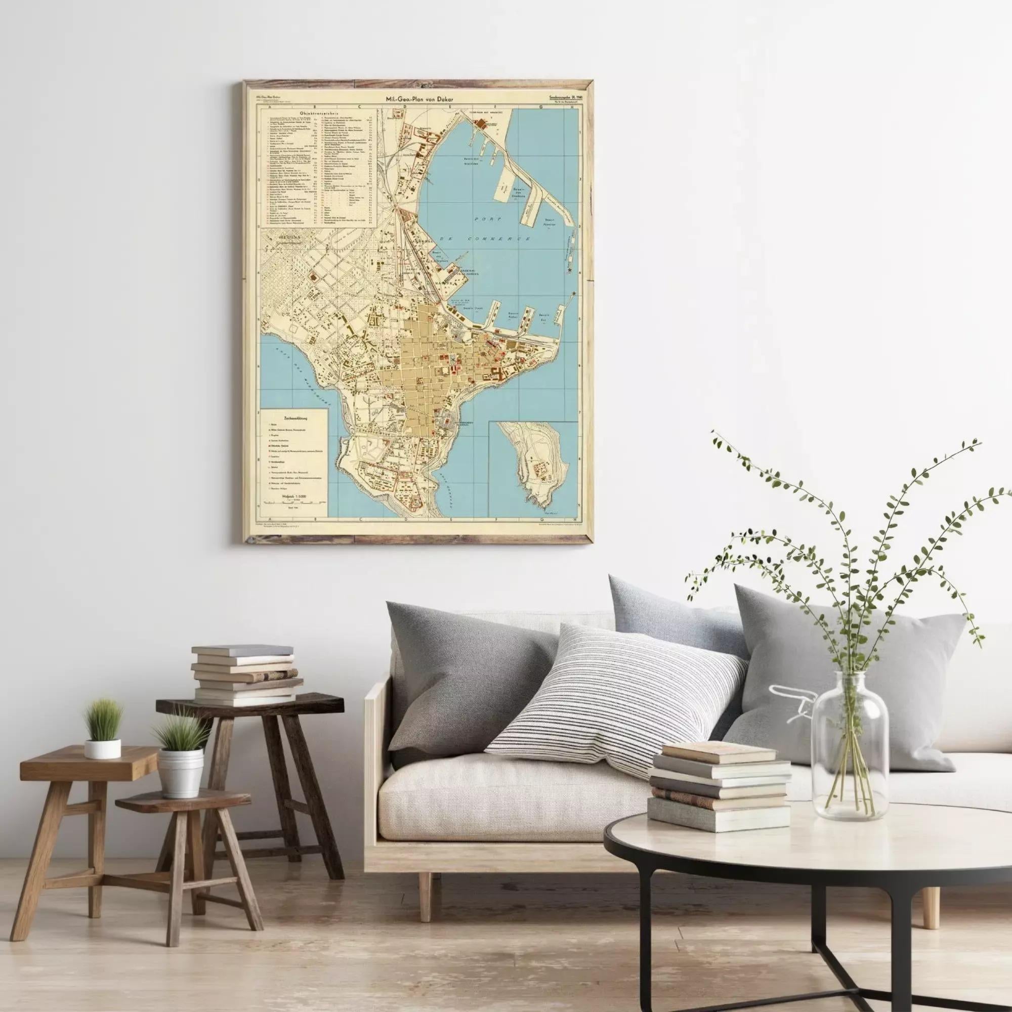 a living room with a large map of a city hanging on the wall, a wooden coffee table with books and a vase of greenery, and a gray sofa with a stack of books on it.