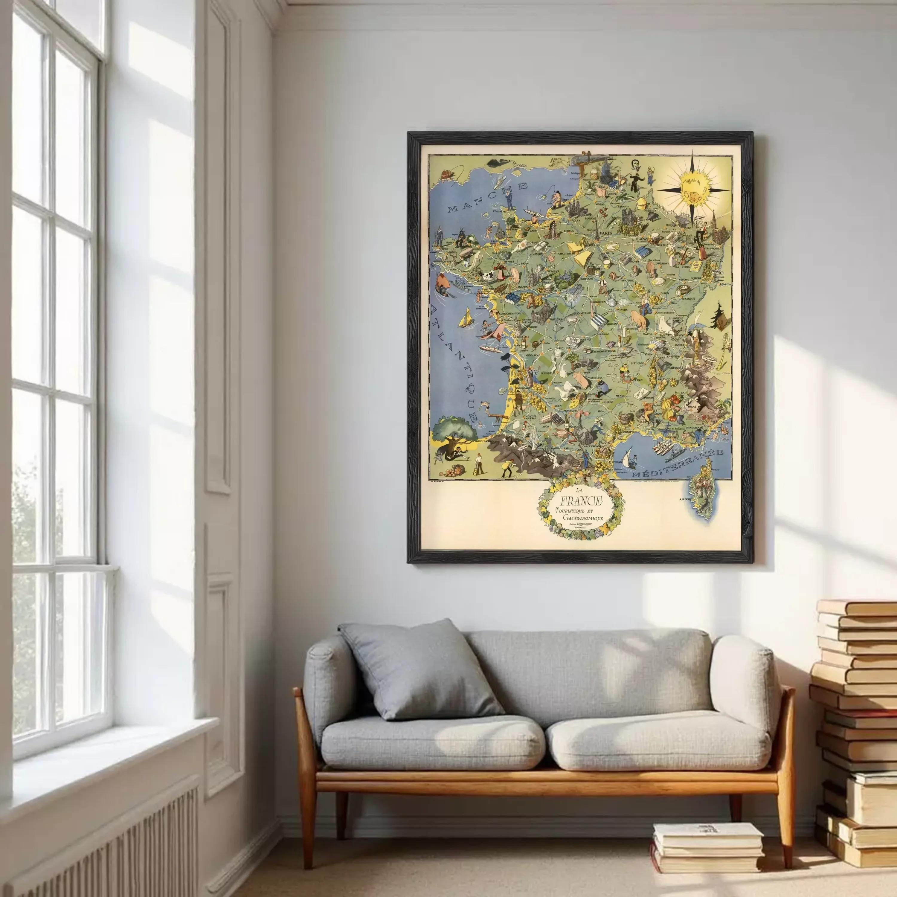 a large framed map of France hanging on a wall, with a gray sofa and a stack of books in the foreground.