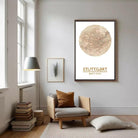 a cozy living room with a large framed map of Stuttgart hanging on the wall, a comfortable chair, a stack of books, and a lamp.