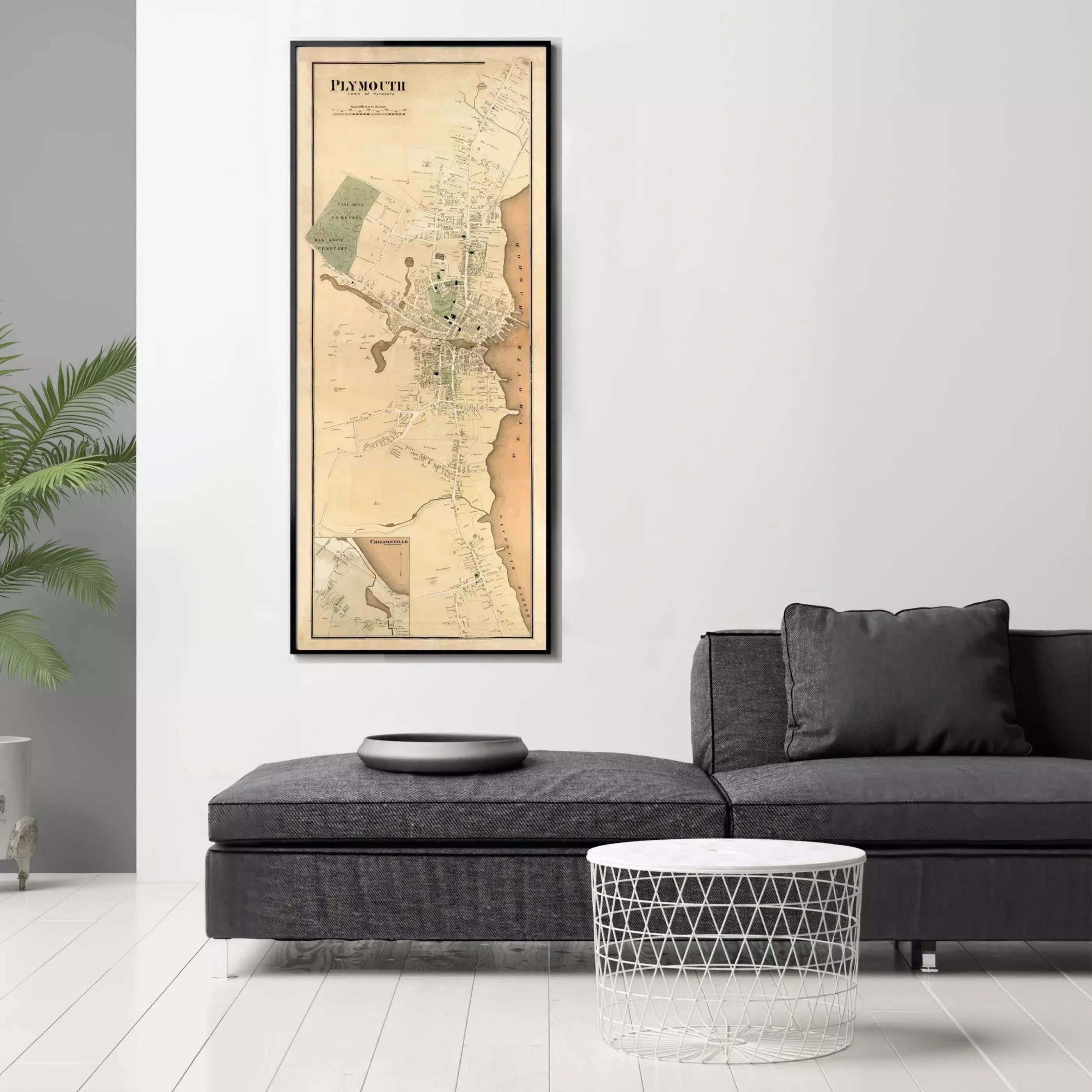 a large framed map of Plymouth, Massachusetts, hanging on a white wall above a black couch and a round table.