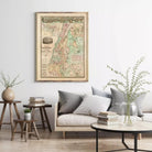 a living room with a large framed map hanging on the wall, a couch with pillows, a coffee table with books and a vase of greenery, and a small table with a plant.