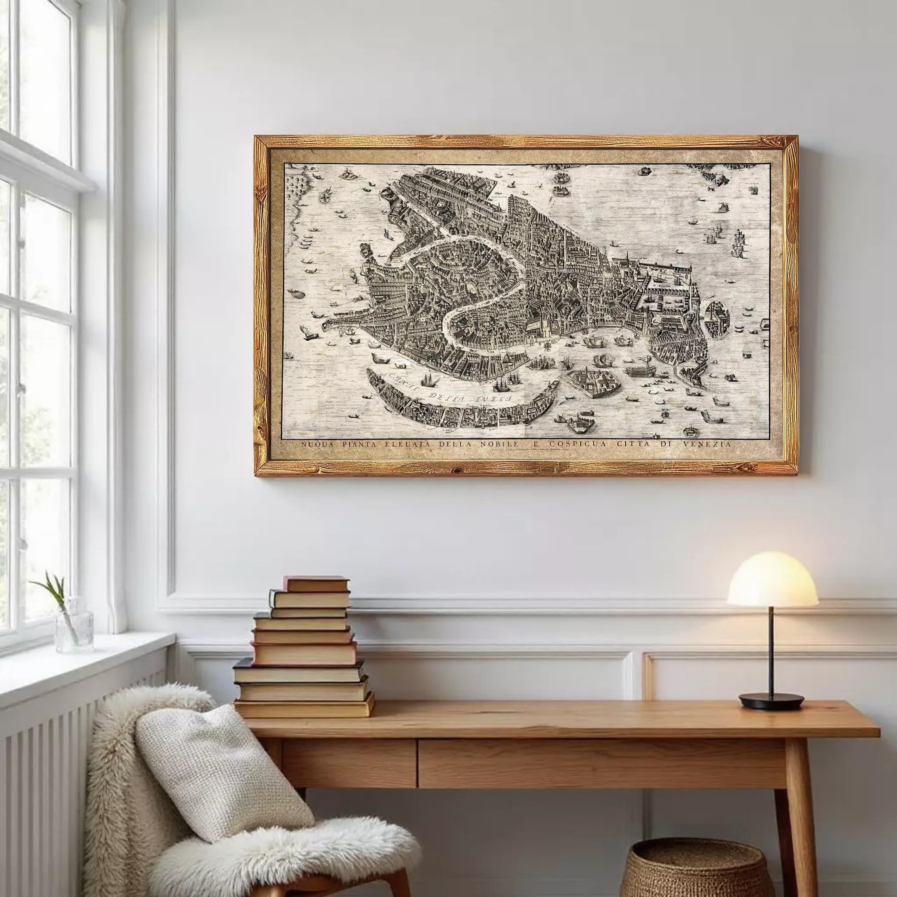 a wooden desk with a stack of books, a lamp, and a framed map of Venice hanging on the wall above it.