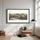 a large black and white framed print of a landscape depicting a countryside scene, hanging on a white wall above a wooden chair and a floor lamp in a well-lit living room.