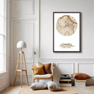 a living room with a large map of Lowell, Massachusetts, hanging on the wall. The room has a white color scheme, with a wooden chair, a lamp, and a stack of books.