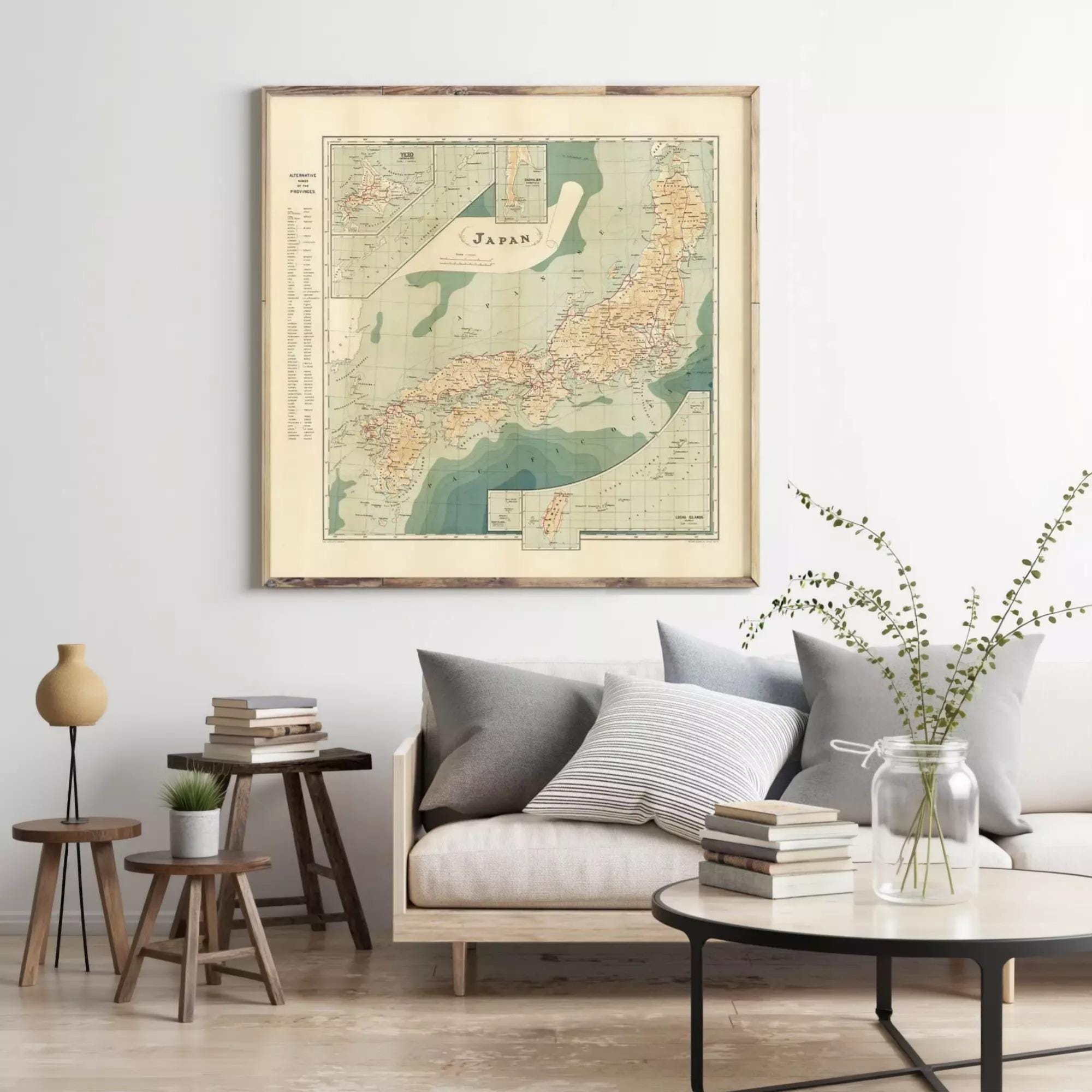 a living room with a large framed map of Japan hanging on the wall above a couch with pillows. The room also includes a coffee table with books and a vase with greenery.